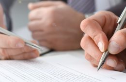 Male arm in suit and tie fill form clipped pad with silver pen closeup. Sign gesture read pact sale agent bank job make note loan credit mortgage investment finance executive chief legal teamwork law